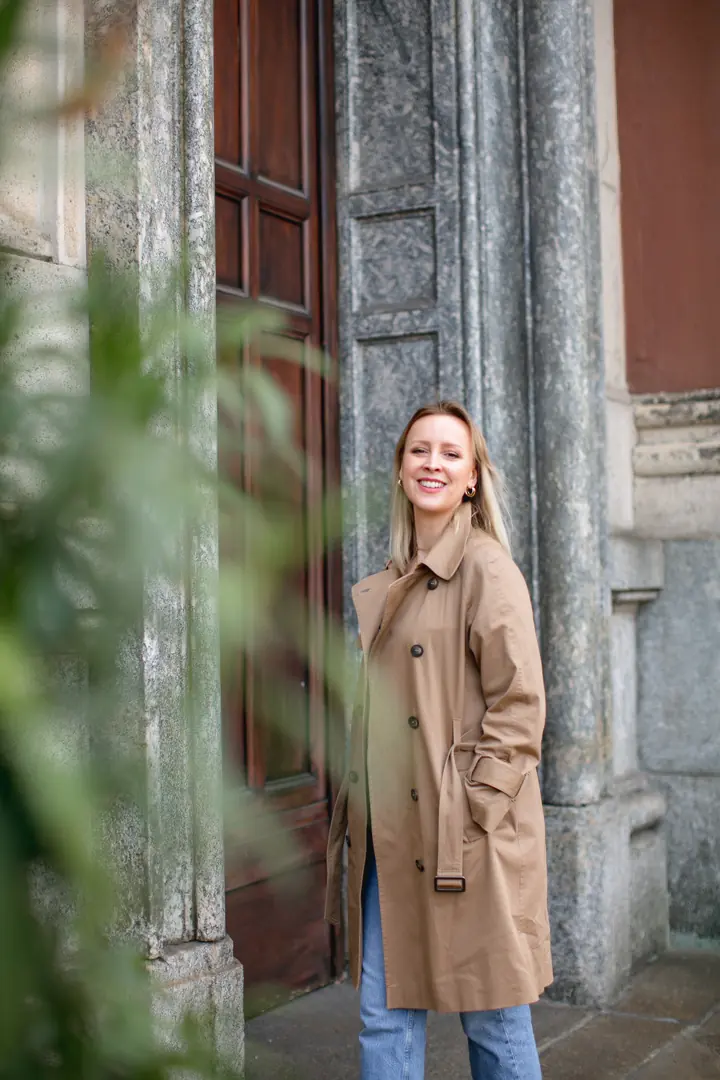 Svitlana in a camel trench coat, smiling in an old stone doorway.